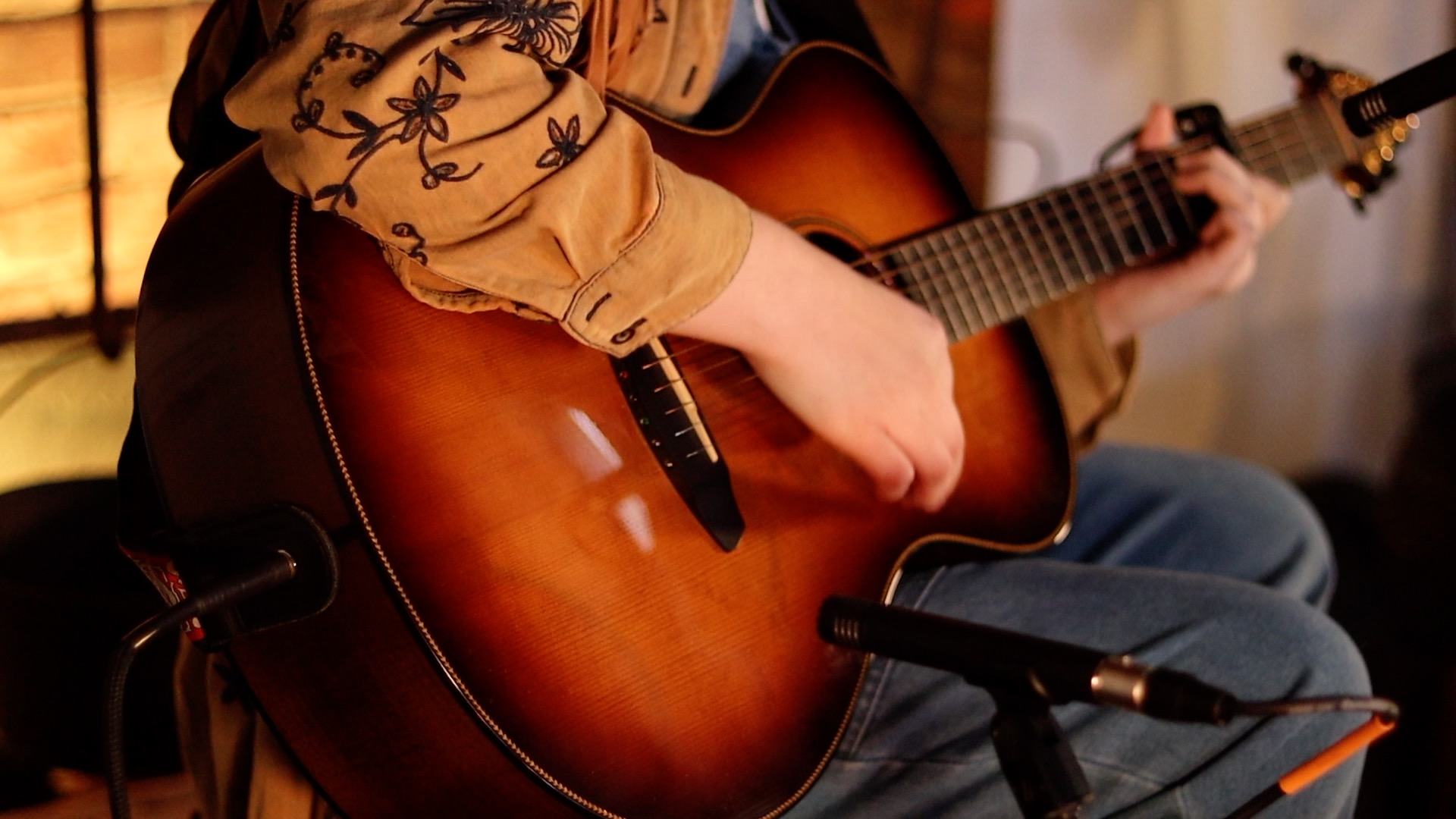 Close up photo of young woman playing an acoustic guitar, miked up for recording in a local museum.